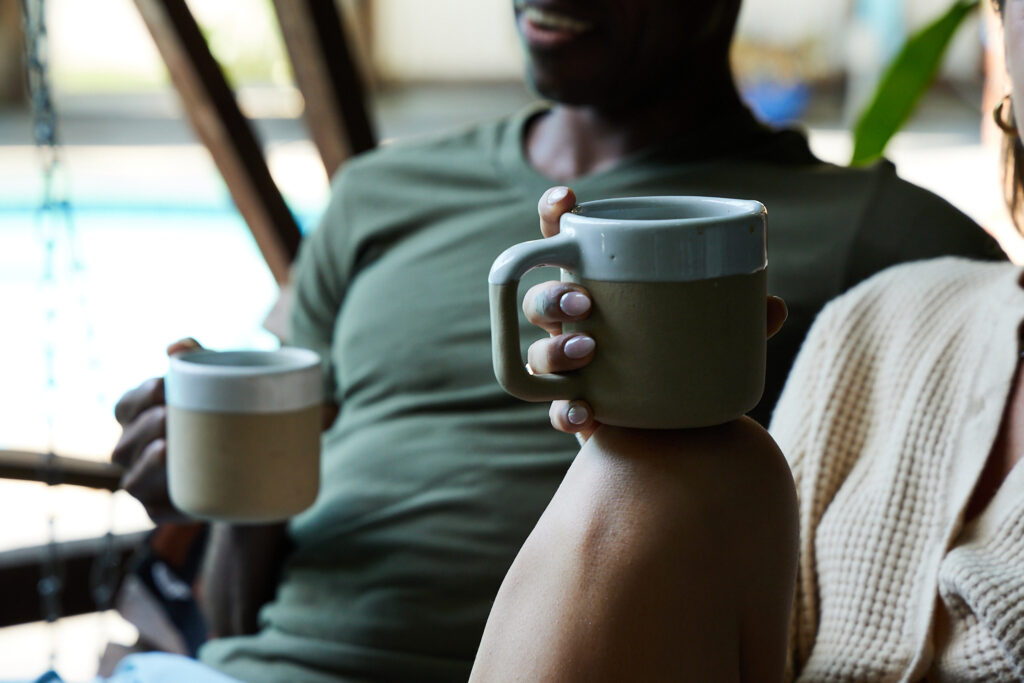 man and woman each having coffee in a stone mug outside. 