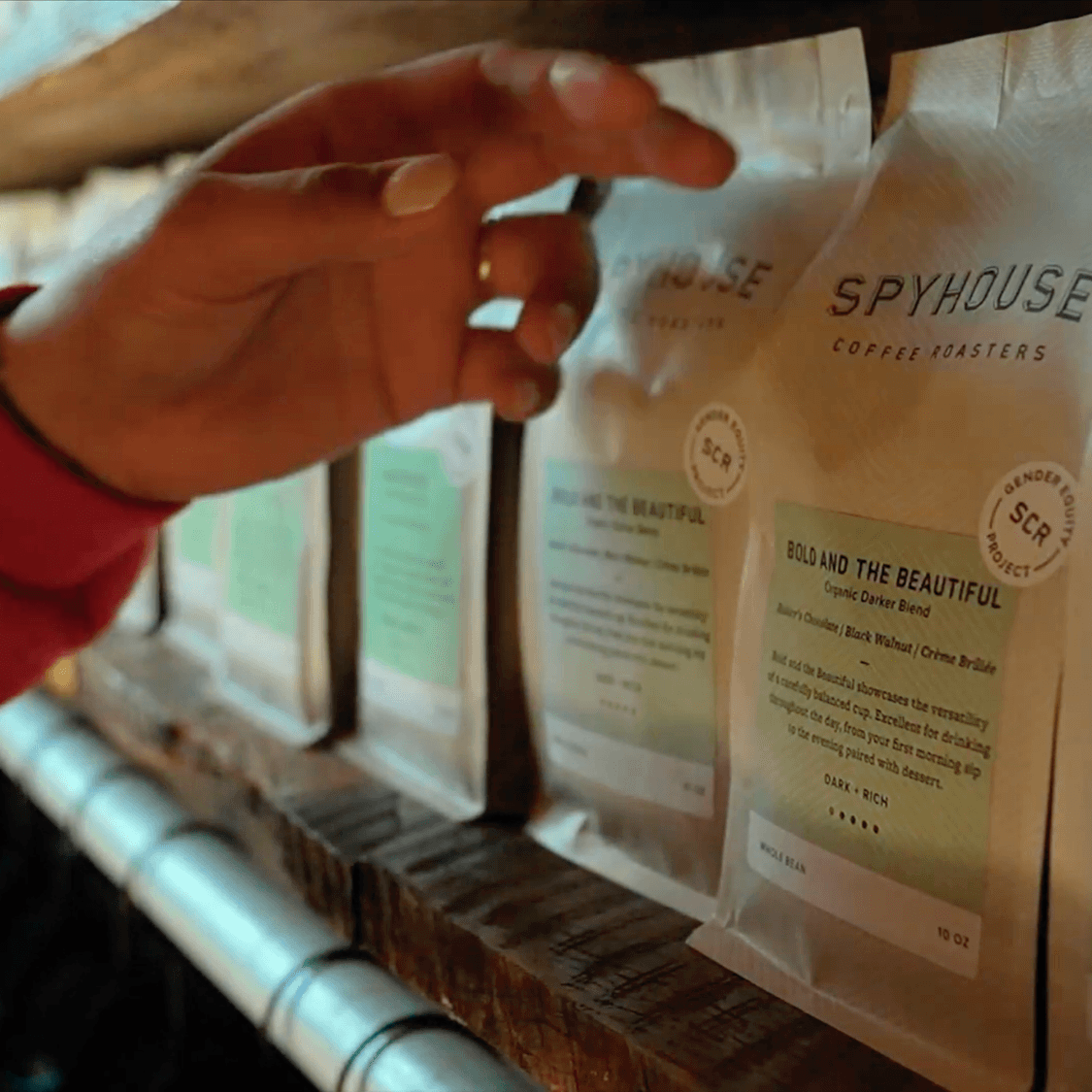 A hand reaches for a bag of Spyhouse Coffee's "Bold and the Beautiful Blend).
